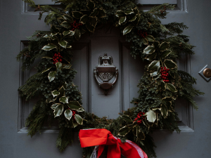 A classic grey front door adorned with a lush holiday wreath made of greenery, holly leaves, and red berries. The wreath is tied with a bright red ribbon, and the door features a silver knocker in the centre, creating a festive and welcoming holiday entrance.