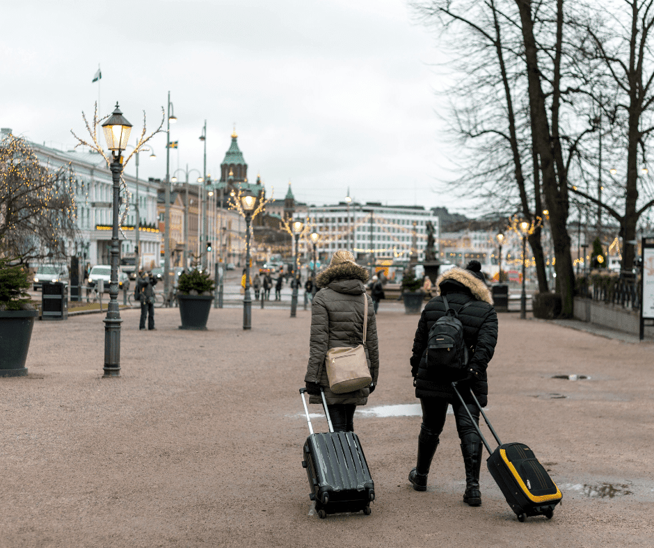 Two travellers in winter coats walking through a European city with suitcases, symbolising the importance of winter travel insurance for safe and protected journeys.
