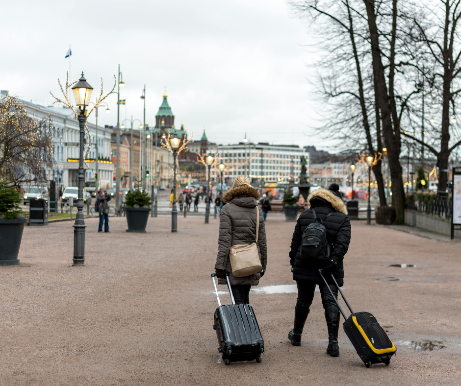 Two travellers in winter coats walking through a European city with suitcases, symbolising the importance of winter travel insurance for safe and protected journeys.
