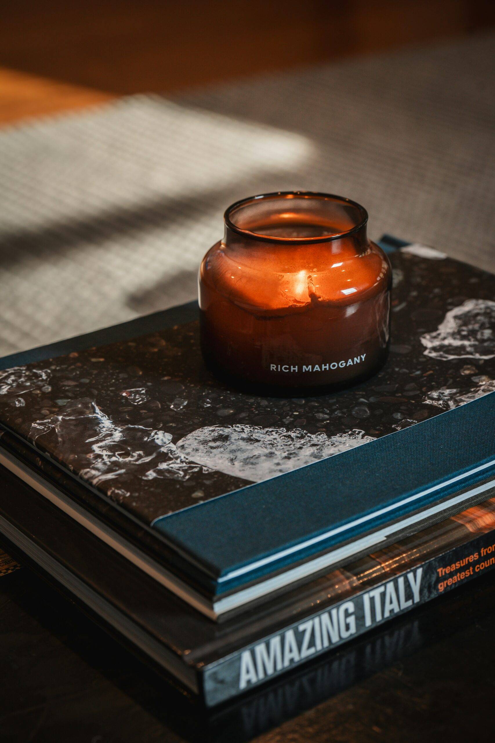 Lit candle in a glass jar resting on a stack of books, used as a reminder of candle fire safety in the home.